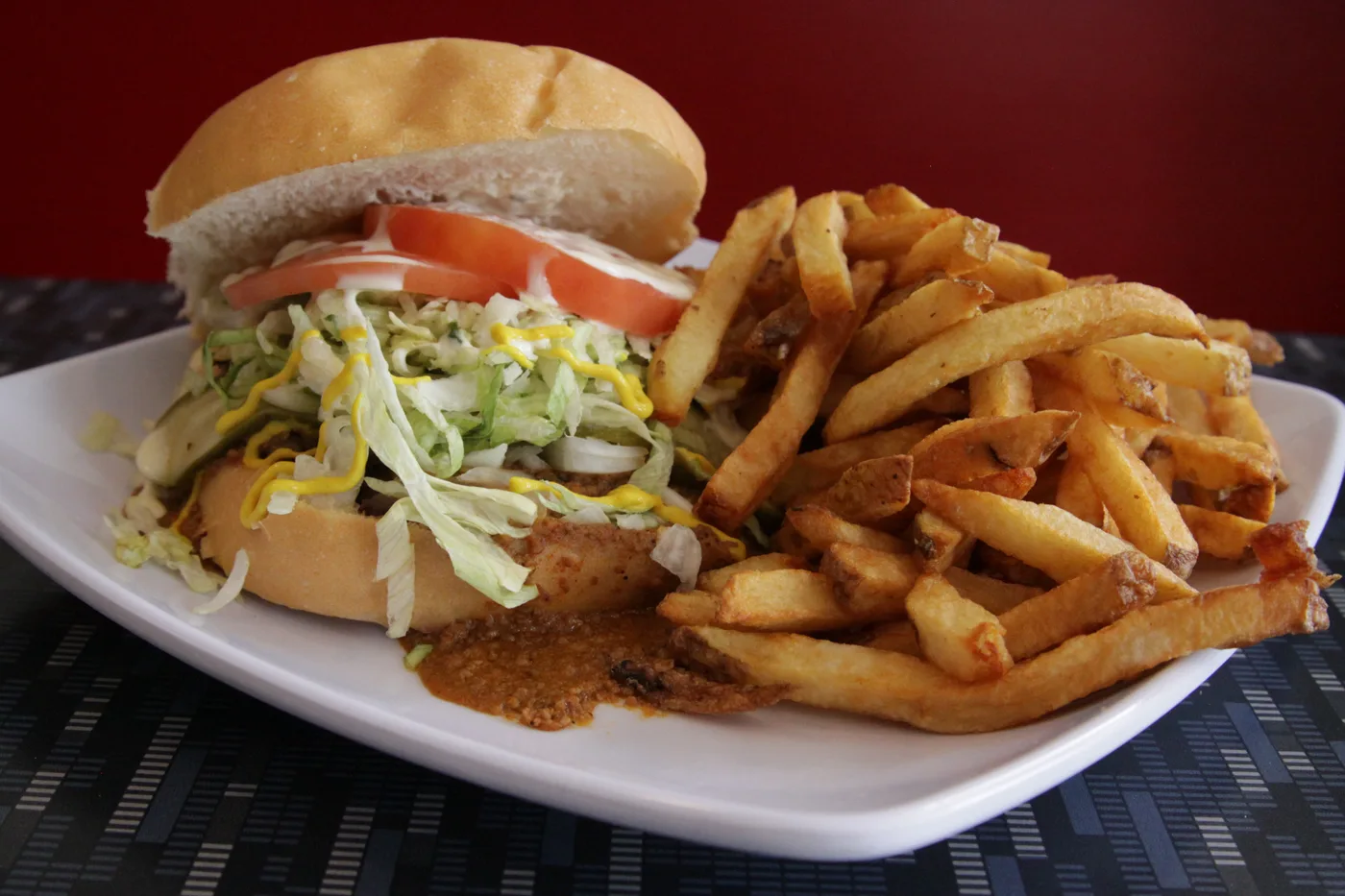 A burger with lettuce, tomato and mustard beside a pile of fries