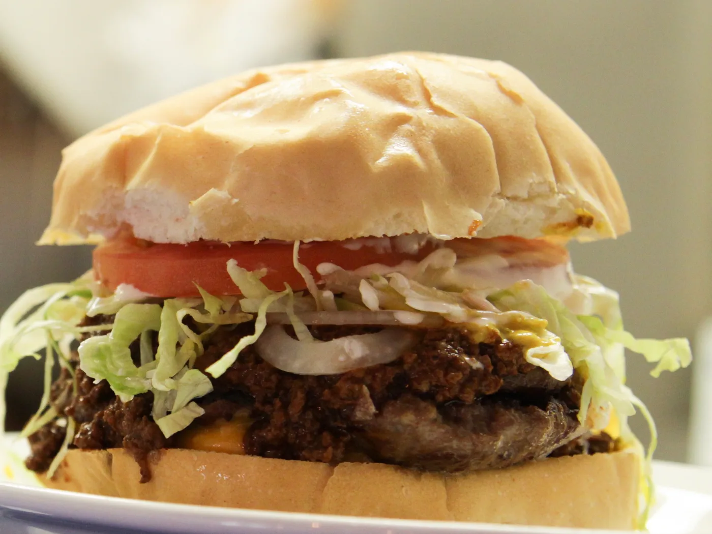 A burger with chili, cheese, onion, lettuce and tomato on a bakery style bun