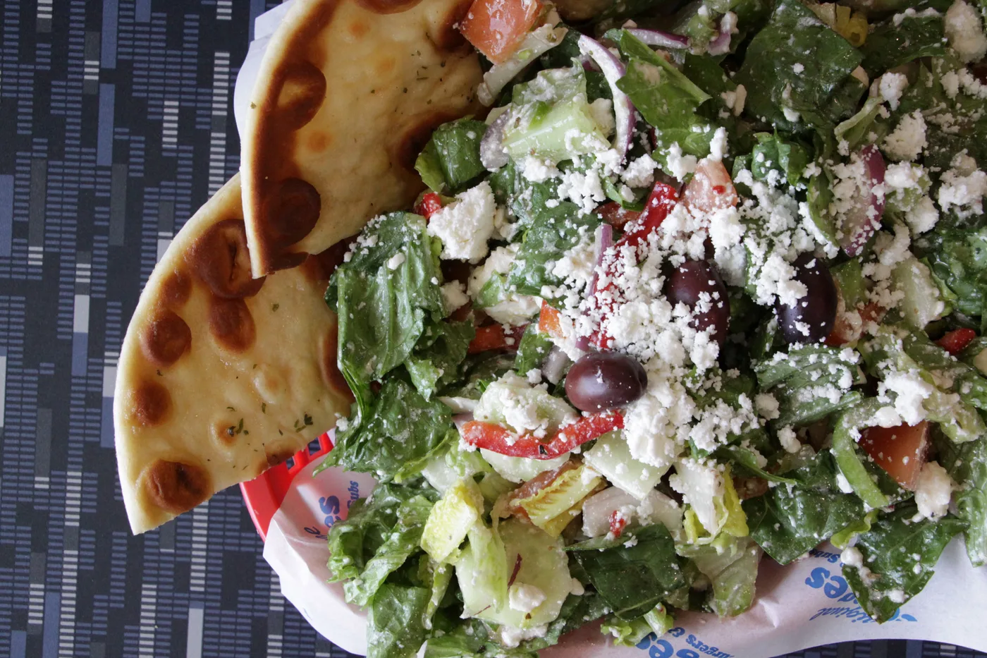 A Greek salad with feta and olives and grilled pita, on a Georges paper liner