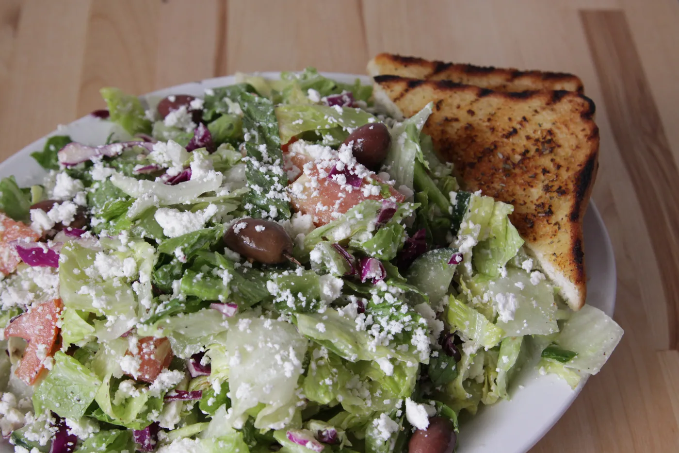 A Greek salad with feta, olives and grilled bread on a wooden table