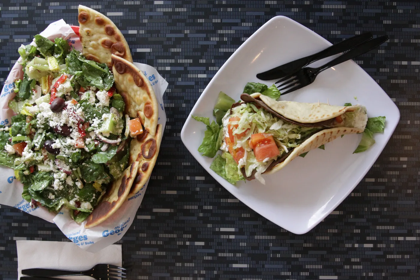 A pita wrap on a plate beside a salad with grilled pita